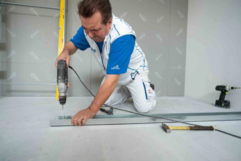 Muž vrtá otvor do sádrokartonu pro instalaci světla.