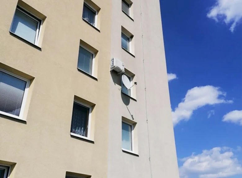 Klimatizační jednotka na fasádě bytového domu pod okny.