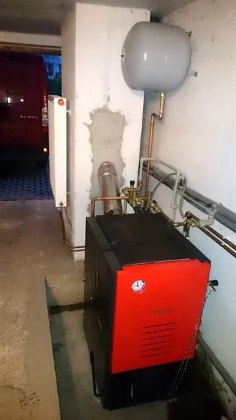 Nový červený plynový kotel instalovaný vedle starého bílého s měděnými potrubími.