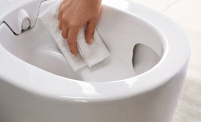 Ruka čistí vnitřní okraj bílé toalety hadříkem.