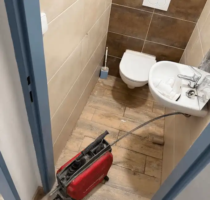 Červený hydraulický hadicový nástroj pro čištění zanesené toalety v koupelně.