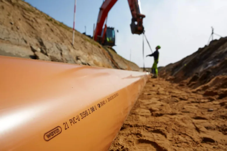 Oranžové kanalizační potrubí z PVC při instalaci v jámě.