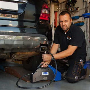 Mechanik kontroluje výfukový systém automobilu v garáži
