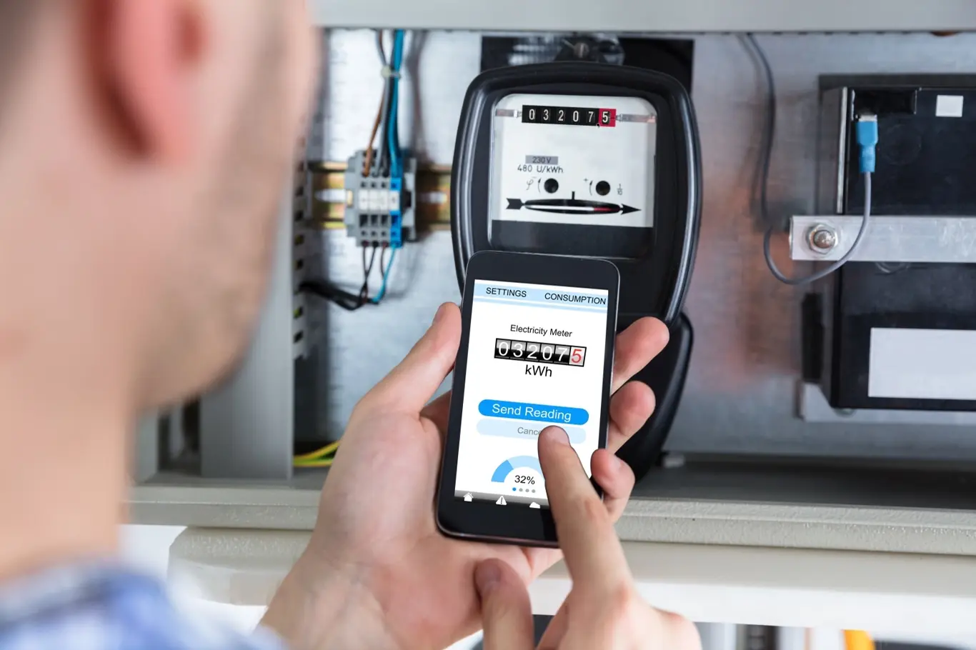 Člověk drží chytrý elektroměr v mobilu u fyzického měřiče.