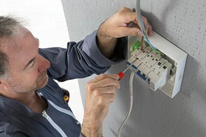 Elektrikář montuje jistič v rozvaděči pro elektrickou instalaci.