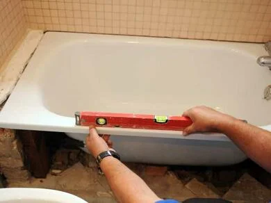 Montážní pracovník kontroluje úroveň instalované vany pomocí hladiny.