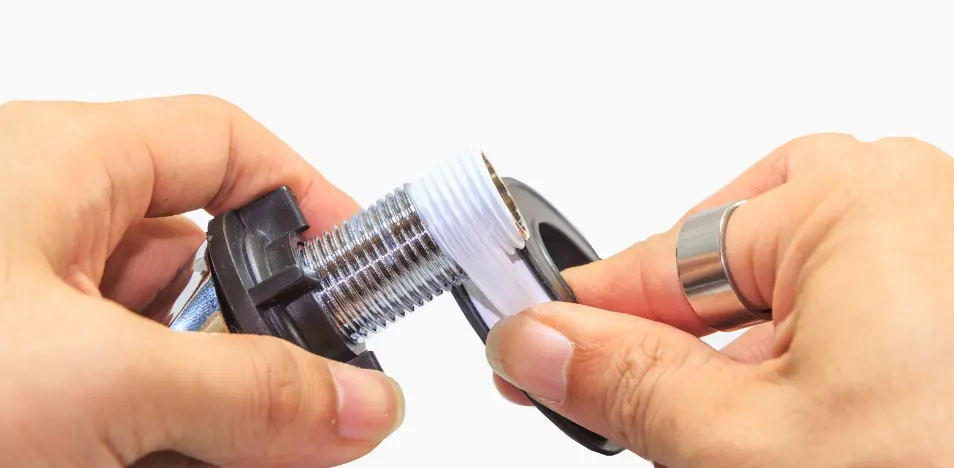 Ruční aplikace bílé utěsnovací pásky na závitové spojení v instalaci.