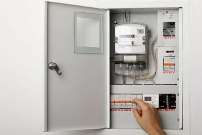 Ruka ukazuje na jistič v rozvaděči s elektroměrem.
