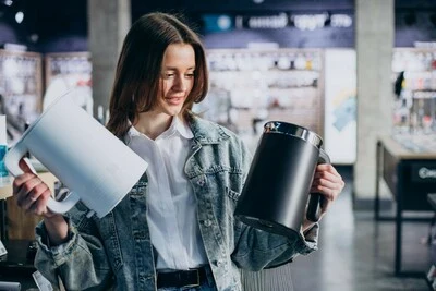 Žena porovnává dvě elektrické konvice v obchodě.