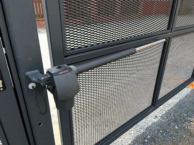 Detailní pohled na zámek automatické brány s mřížkou.
