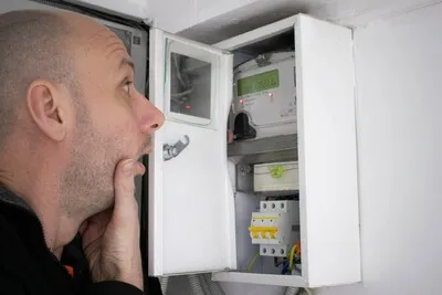 Muž zkoumá elektroměr v rozbitém elektrickém rozvaděči.