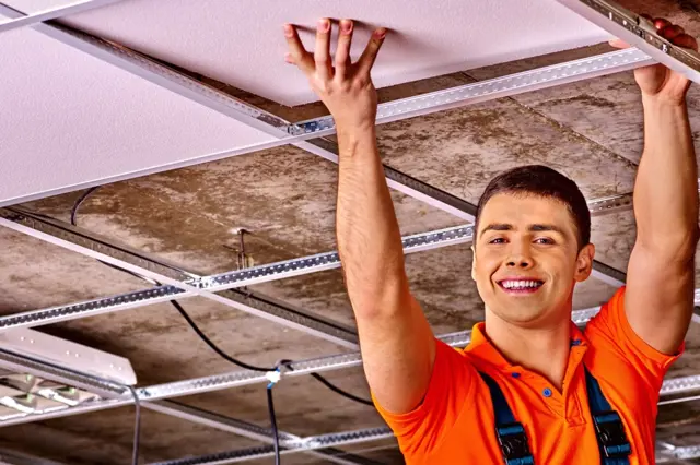 Montážník zvedá stropní desku nad elektroinstalací pod zavěšeným stropem.