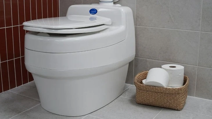 Bílý suchý záchod vedle košíku s toaletním papírem.