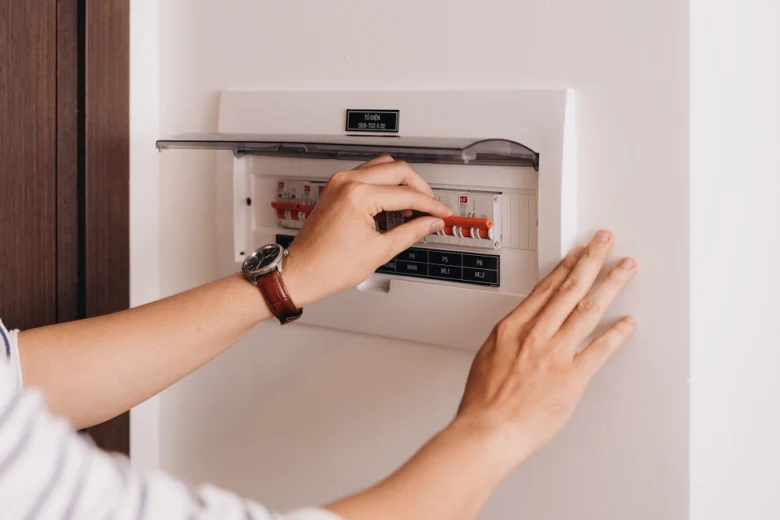 Ruka přepíná jistič v rozvaděči před elektroměrem.