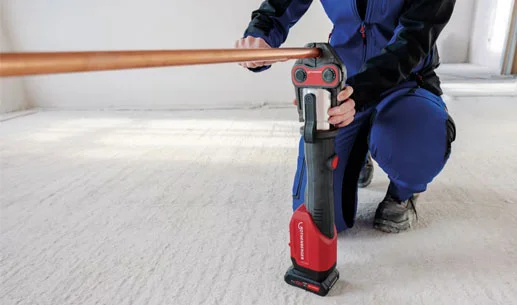 Instalatér lisuje měděnou trubku pomocí elektrického nástroje.
