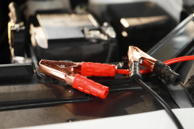 Připojení červených a černých kabelů k autobaterii v motorovém prostoru.