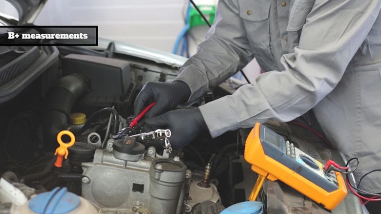 Mechanik měří napětí v motoru multimetrem při diagnostice.