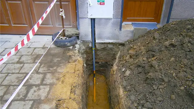 Vykopaná jáma s viditelným žlutě označeným plynovým potrubím vedoucím k domu.