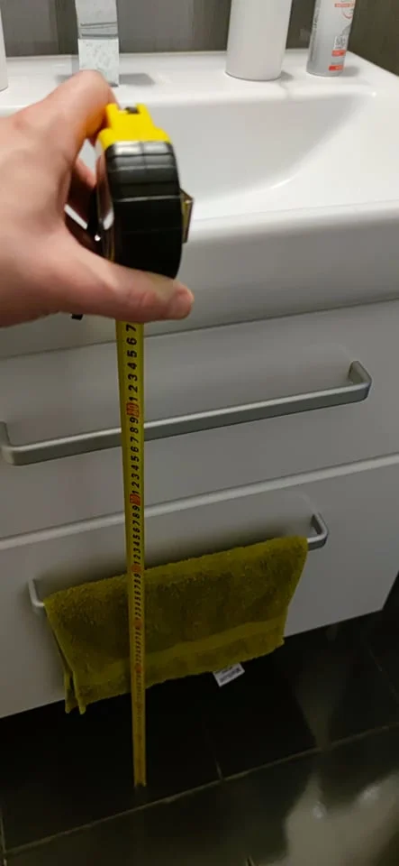 Ruční měření výšky umyvadla páskou vedle skříně