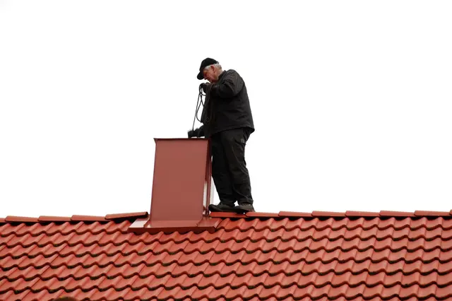 Muž na střeše u komínové klapky s nástrojem.