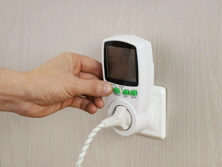 Ruka tlačí na měřič spotřeby energie v zásuvce.