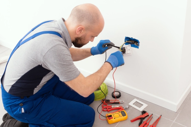 Elektrikář opravuje instalaci v domě pomocí multimetru.