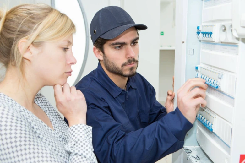 Elektrikář ukazuje jistič v rozvaděči ženě.