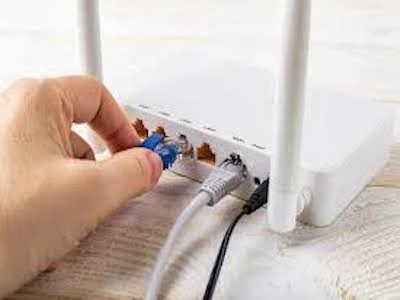 Ruka zapojuje síťový kabel do portu na Wi-Fi routěru.