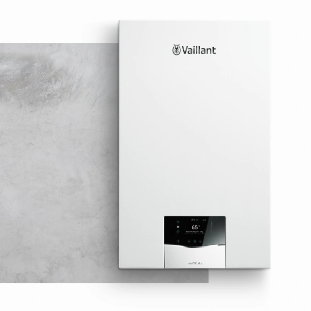 Modern bílý plynový kotel značky Vaillant na šedé zdi.