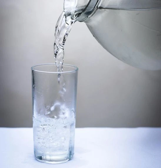 Voda se nalévá do sklenice z konvice na bílém podkladě.