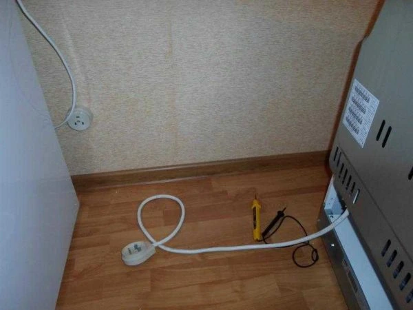 Bílý kabel s zástrčkou u elektrické trouby na dřevěné podlaze.