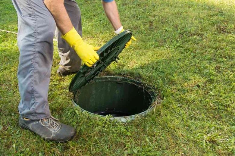 Muž v žlutých rukavicích zavírá víko septiku na trávníku.