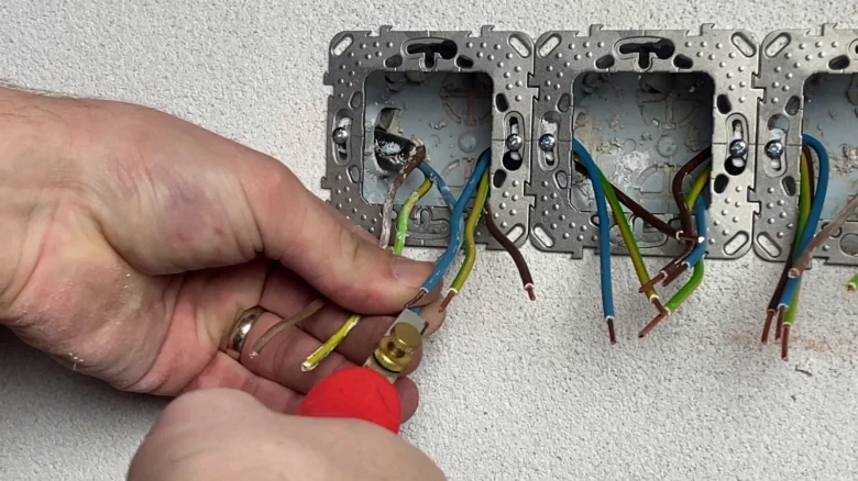 Ruka připojuje vodiče do elektrické zásuvky na zdi.