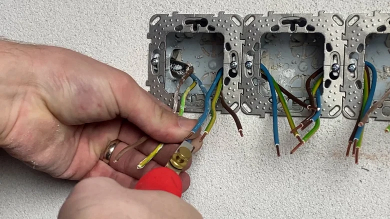 Ruka zapojuje dráty do elektrické zásuvky na zdi.