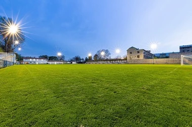Zelené fotbalové hřiště s výkonným osvětlením v době soumraku.