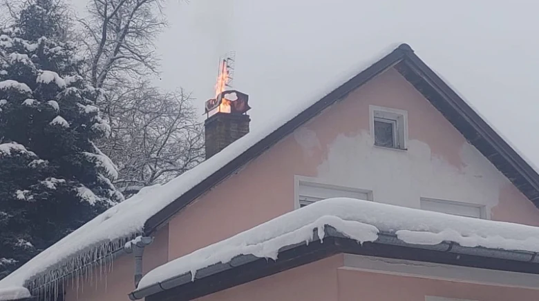 Komín hoří v zimě s jasnými plameny a sněhem na střechách.