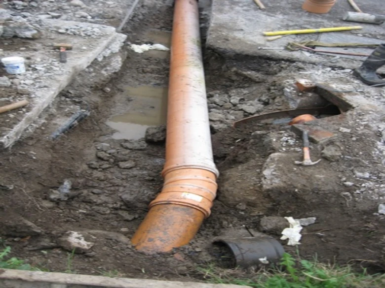 Instalace kanalizační trubice v jámě s nástroji na stavbě.