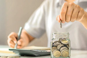 Osoba ukládá mince do sklenice jako součást finančního plánování.
