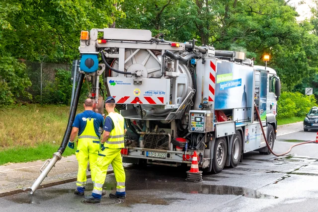 Dva pracovníci u velkého vakuového vozu pro čištění septiků na silnici.