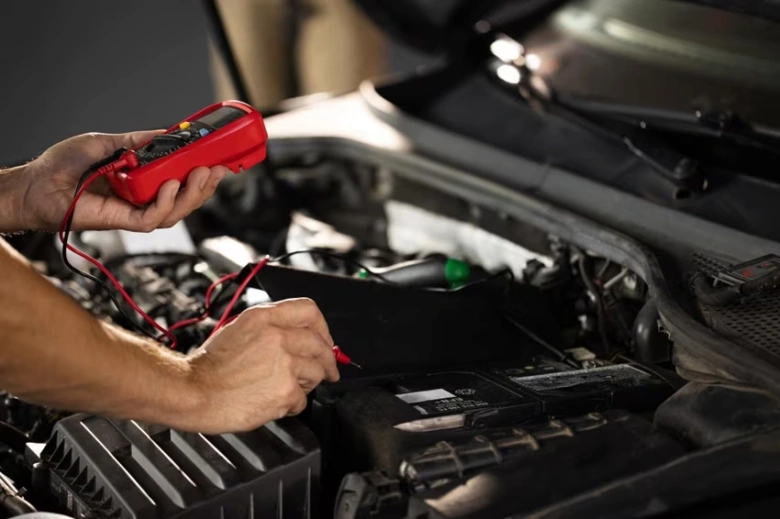 Mechanik měří napětí autobaterie multimetrem pod kapotou auta.