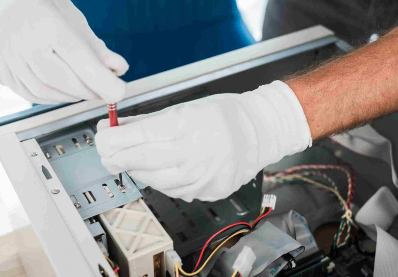 Ruce v bílých rukavicích opravují elektroniku šroubovákem.