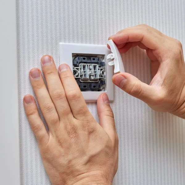 ruce montují bílý elektrický spínač na stěnu