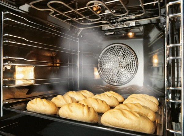 Zlaté chleby pečou v troubě s viditelným konvekčním ventilátorem.