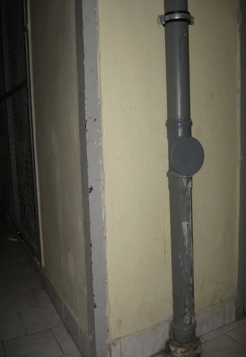Svislá kanalizační stoupačka uvnitř bytu podél zdi.