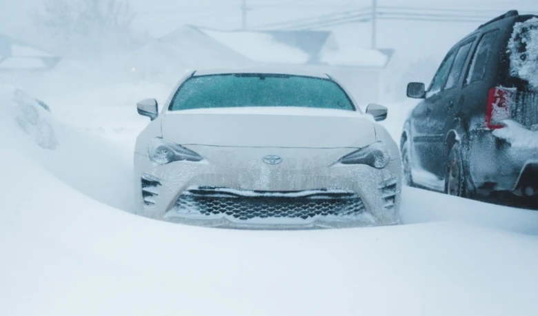 Bílý automobil pokrytý sněhem v zimní bouři na ulici.