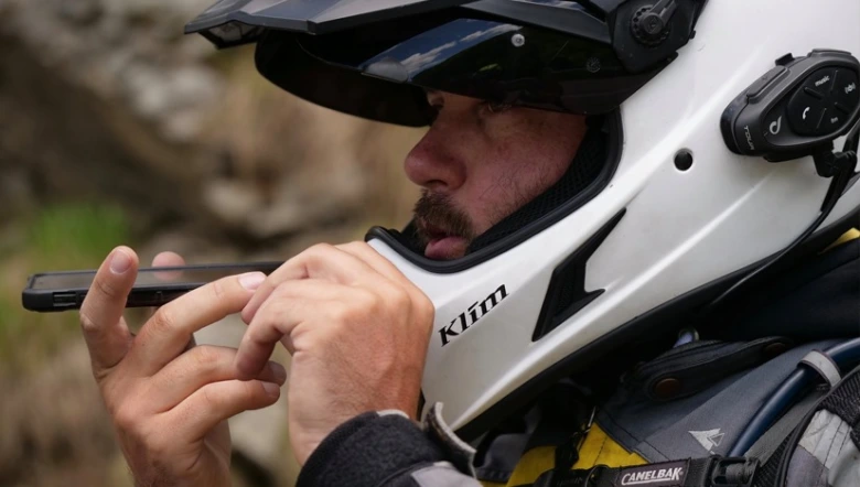 Motocyklista s interkomem v helmetu drží chytrý telefon.