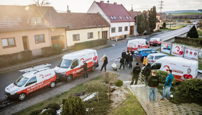 Pracovníci montují klimatizaci na venkovské ulici s firmovými vozy.