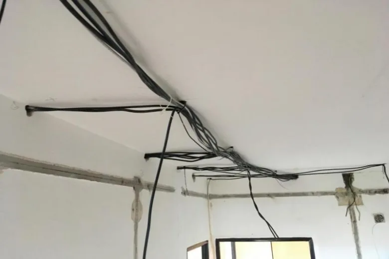 Zamotané elektrické kabely v koutě stropu panelového domu.