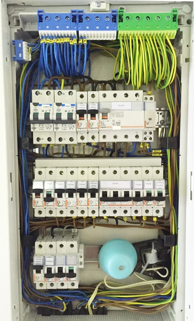 Otevřená elektrická rozvaděč s kabely a pojistkami uvnitř skříňky.