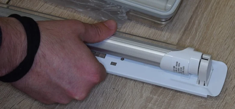 Ruka drží LED lampu pro náhradu zářivky v držáku.